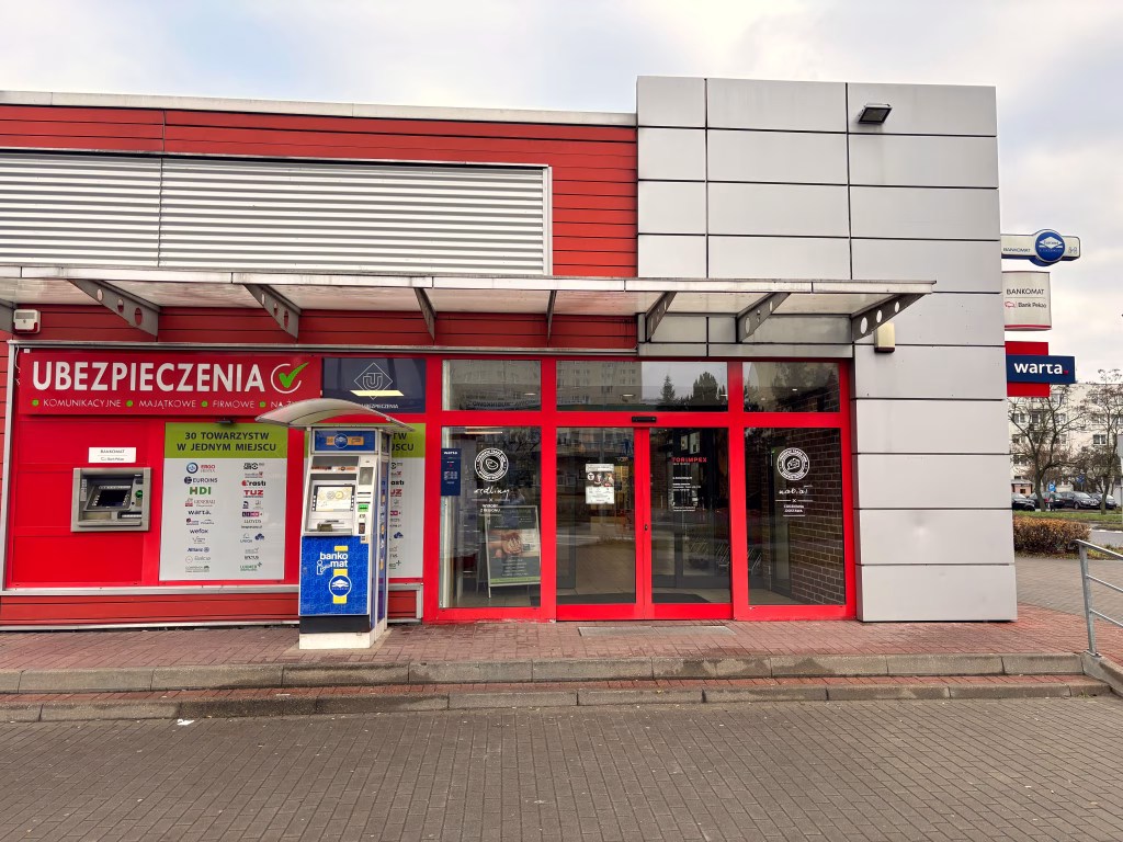 Biuro UTPS Ubezpieczenia, z banerem reklamowym ubezpieczenia, budynek jest z elewacją blaszaną w kolorach stalowym i czerwonym.